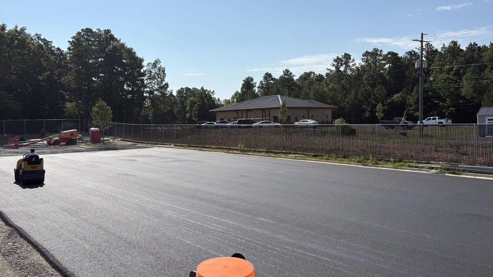 Roller finishing a wide sheet of fresh asphalt on a commercial lot
