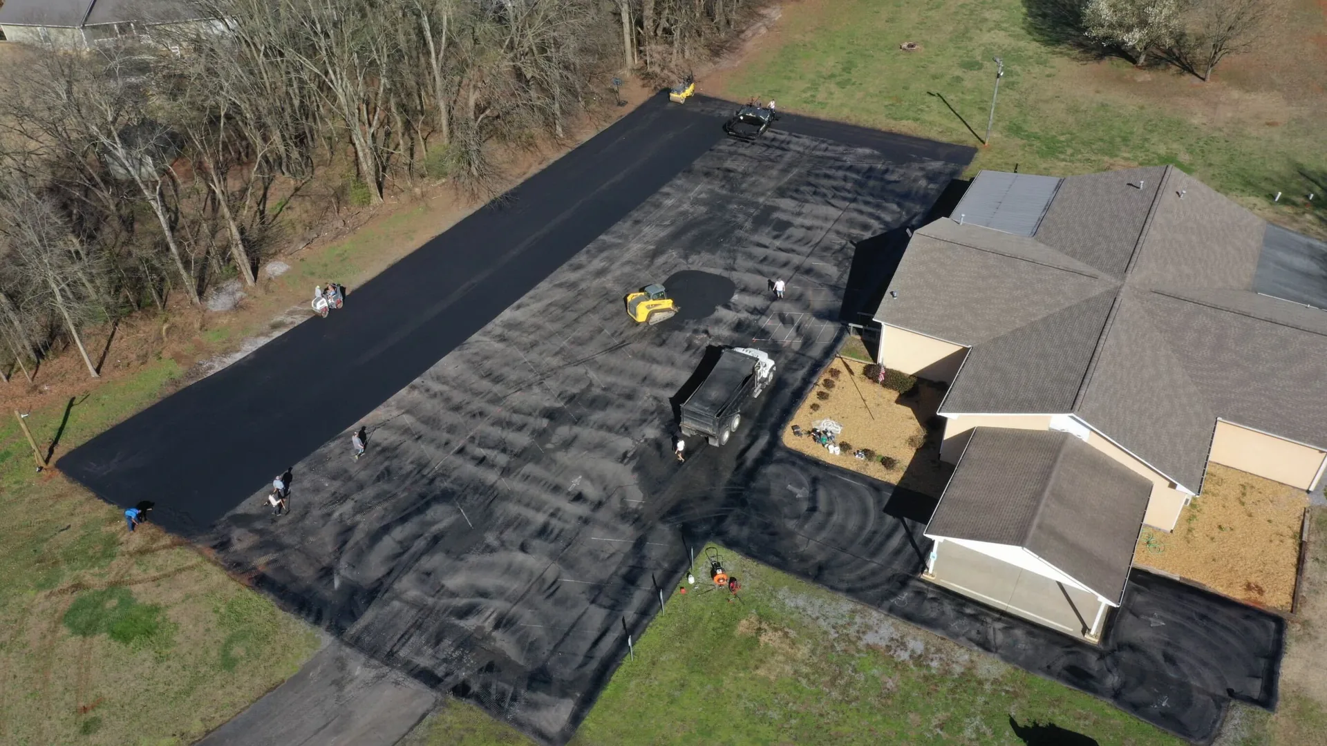 Aerial view of a crew paving a large asphalt drive and parking area beside a home