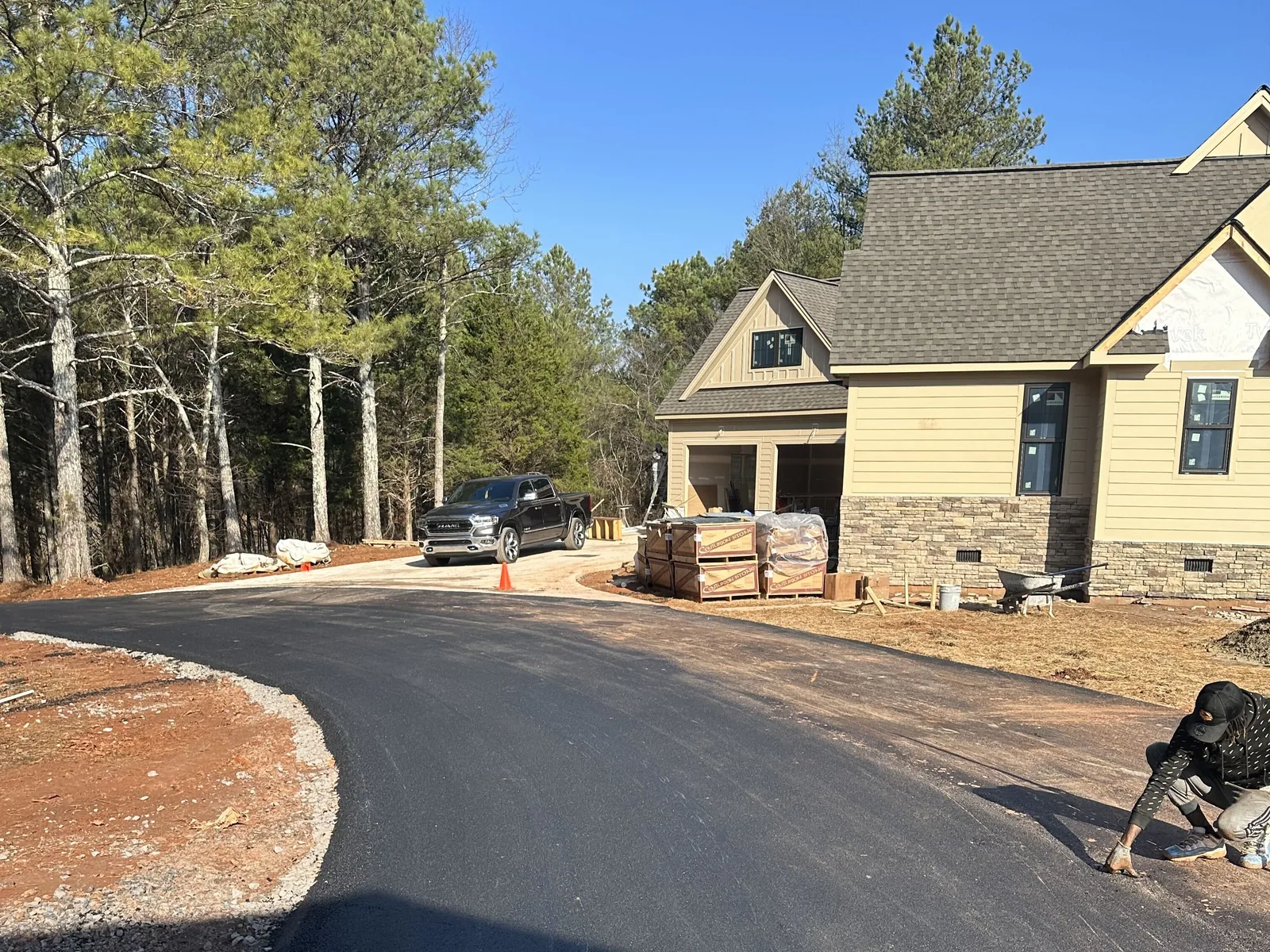 New asphalt driveway curving in front of a house under construction with red clay on both sides