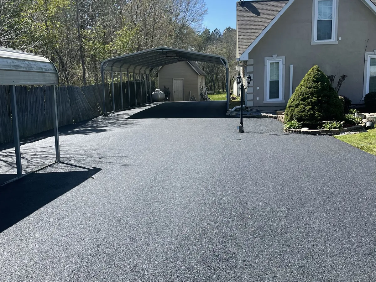 Wide asphalt driveway and parking pad running past a carport at a house