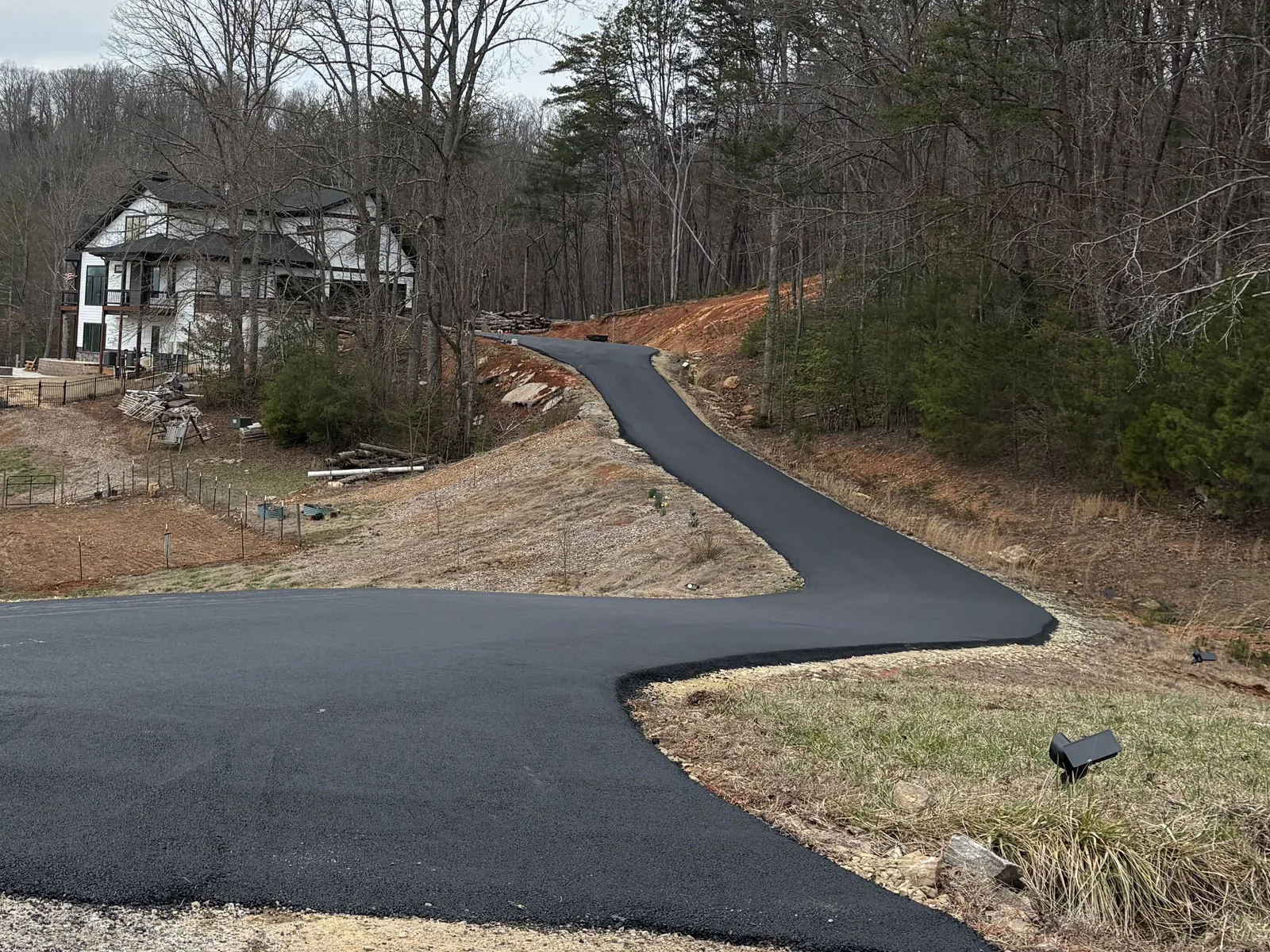 New asphalt drive in the foreground with a lane climbing the hill to a home in the mountains