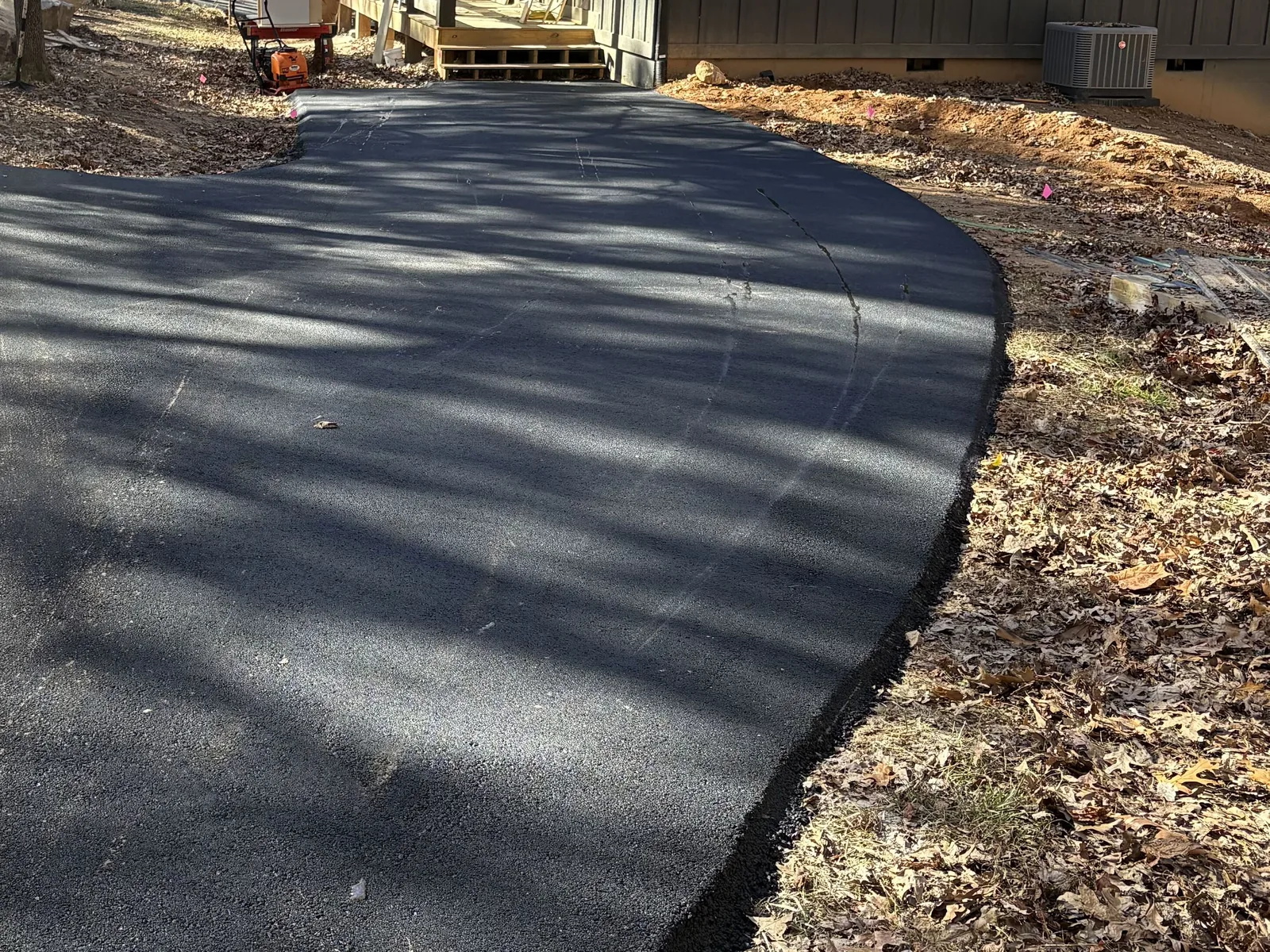 Fresh asphalt parking pad curving up to a dark board and batten cabin