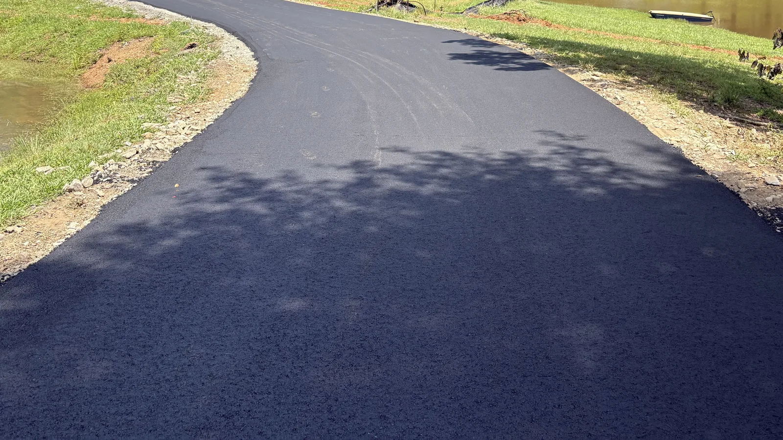 Broad new asphalt drive running between two ponds on a landscaped property