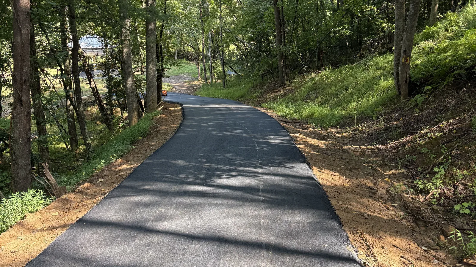 Asphalt paving in Blue Ridge, GA: a fresh asphalt lane climbing through hardwood woods with graded dirt shoulders on both sides