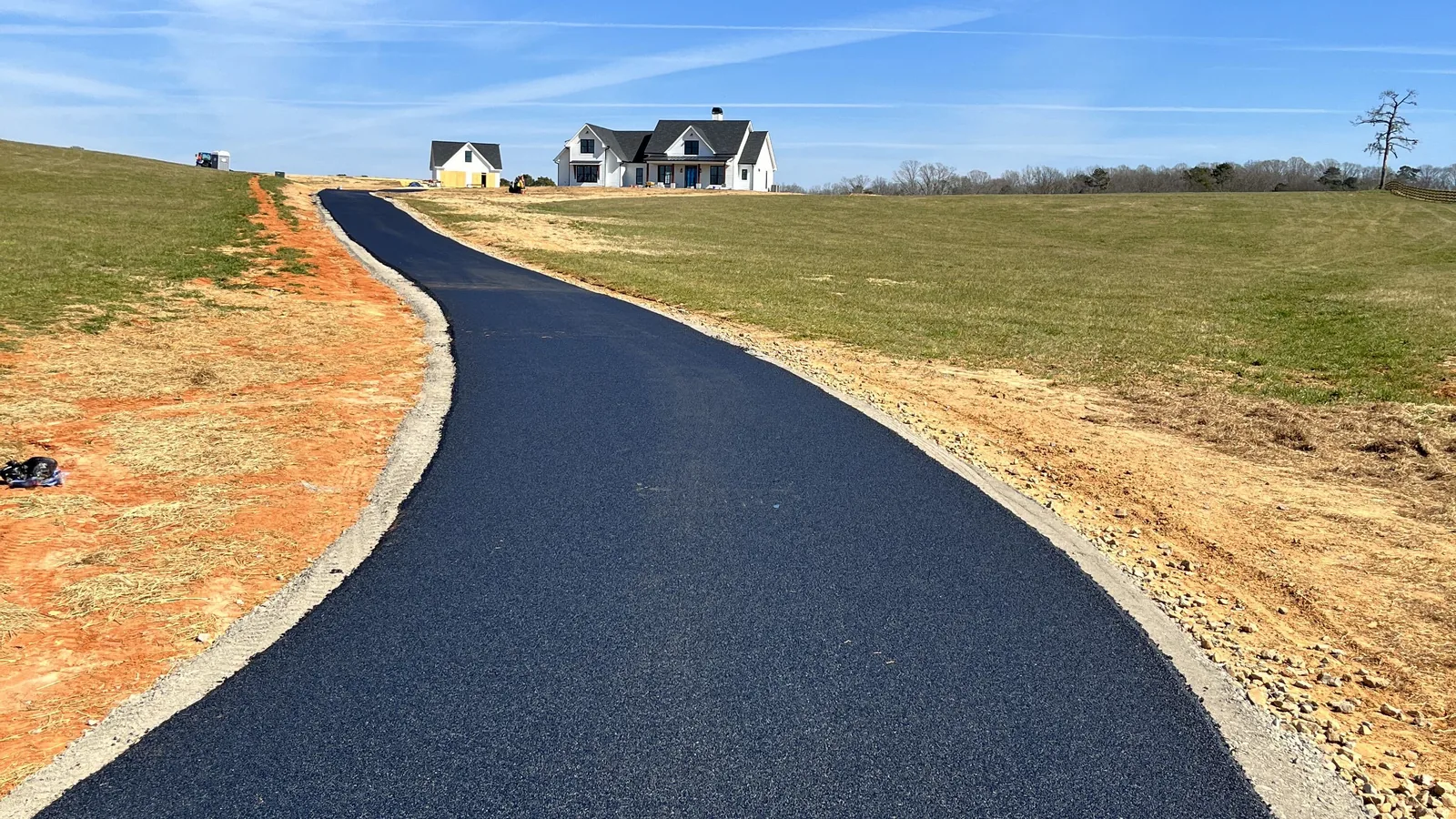 Long black asphalt driveway climbing a pasture toward a white farmhouse