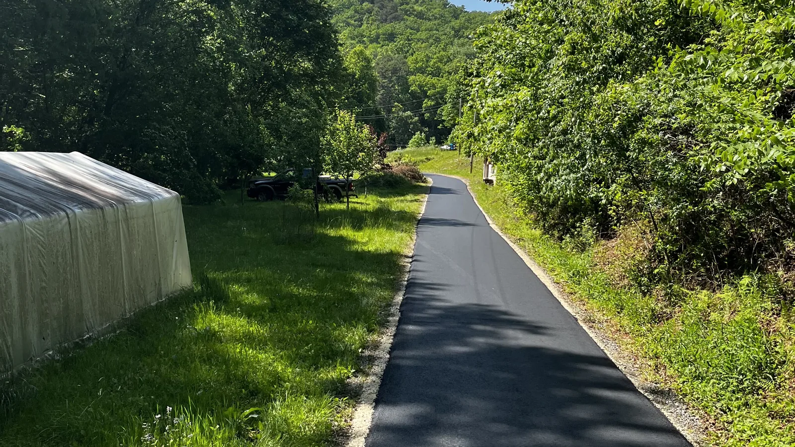 Fresh asphalt drive running down a valley toward a wooded ridge