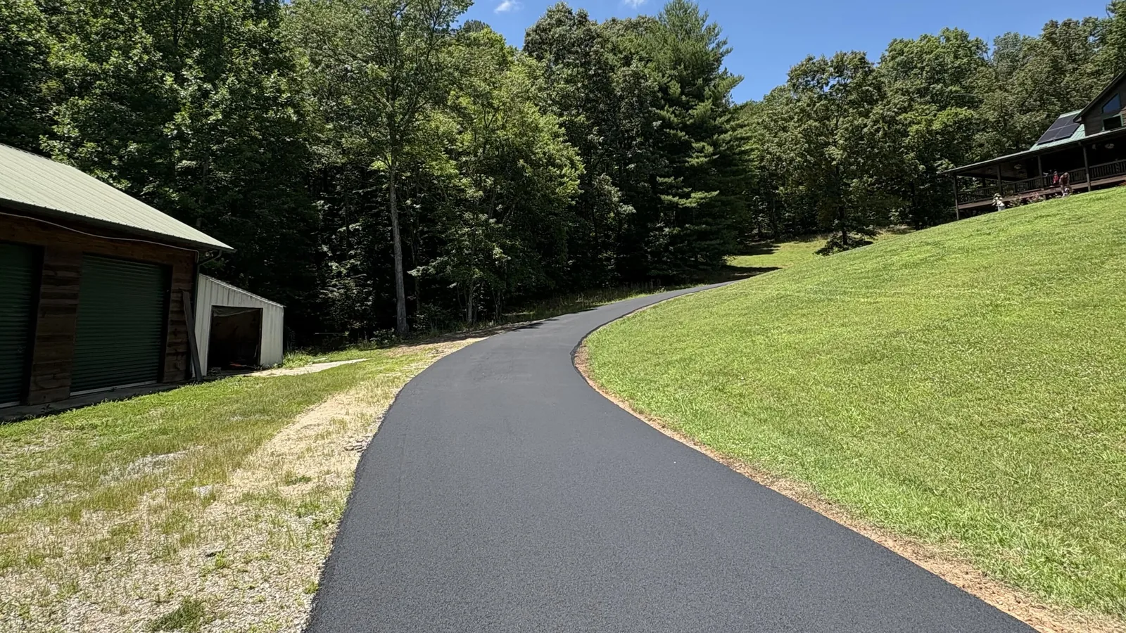 New asphalt driveway curving up a grassy slope past an outbuilding