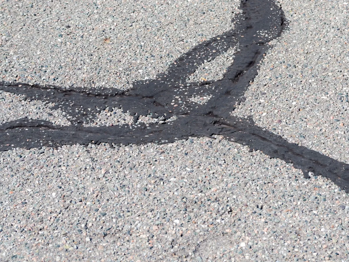 Black crack sealant filling cracks across a gray asphalt surface