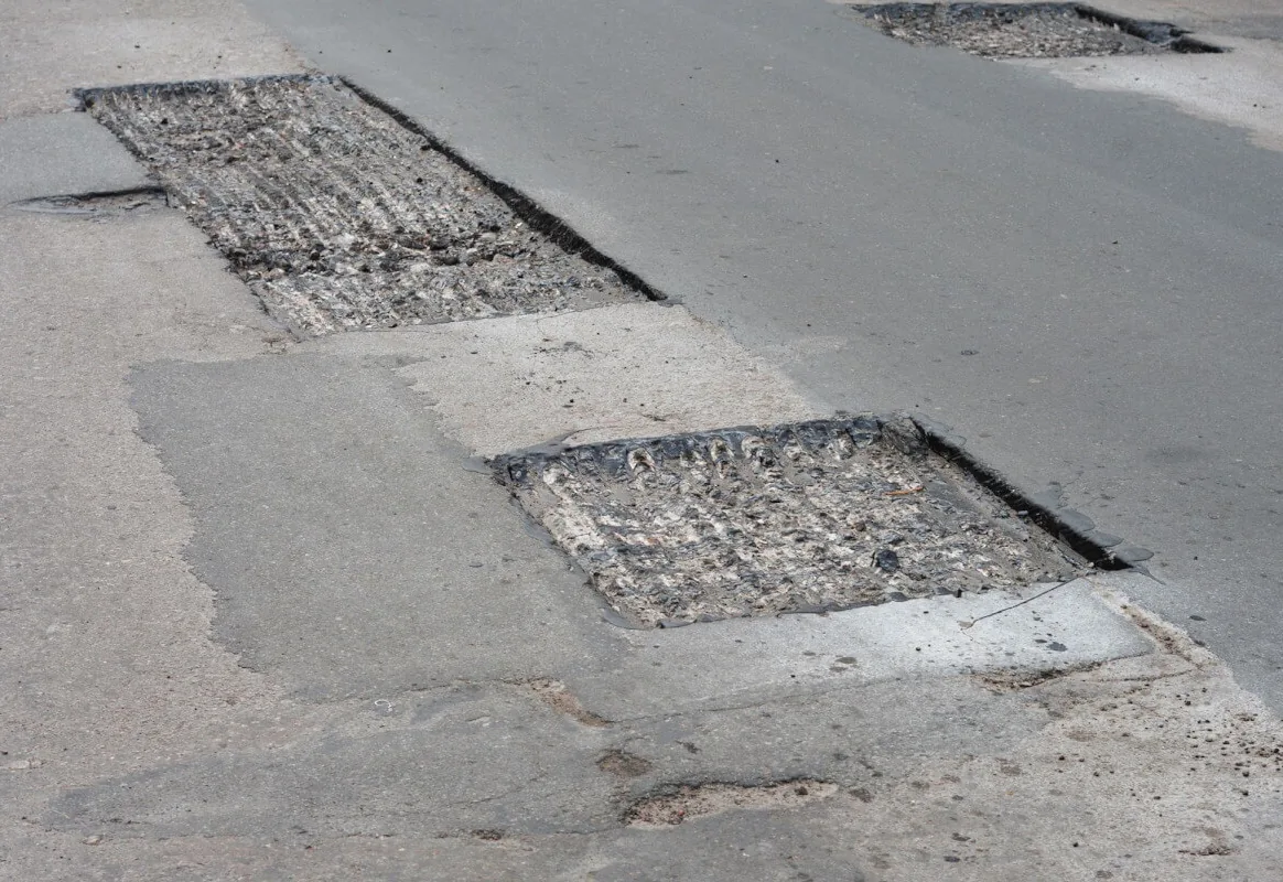 Square cut-out patch areas in an old asphalt lot with the failed surface removed