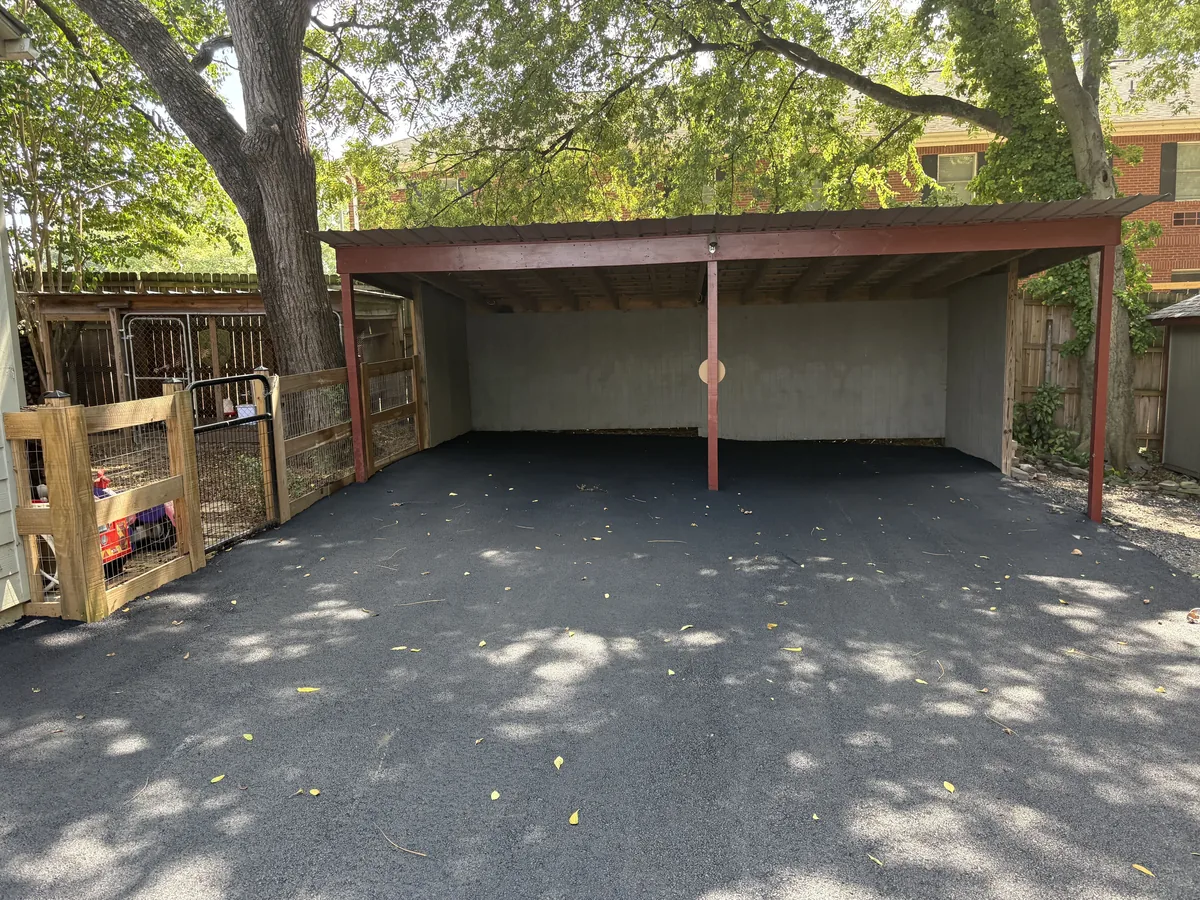 Freshly resurfaced asphalt running in under a carport at a house
