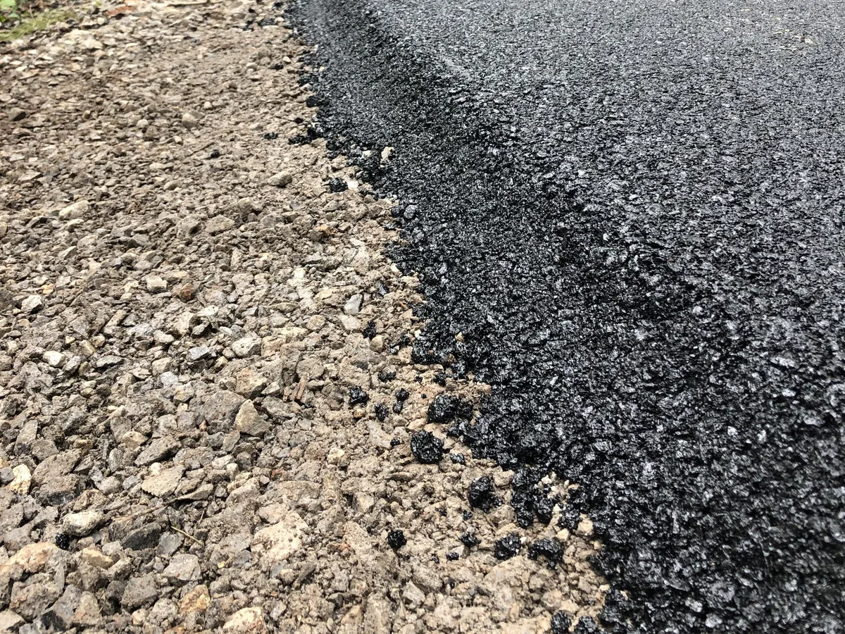 Close view of the edge of a new asphalt layer showing its thickness over the stone base