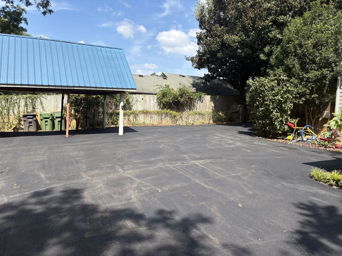 Resurfaced asphalt parking area with a smooth new black surface beside a carport
