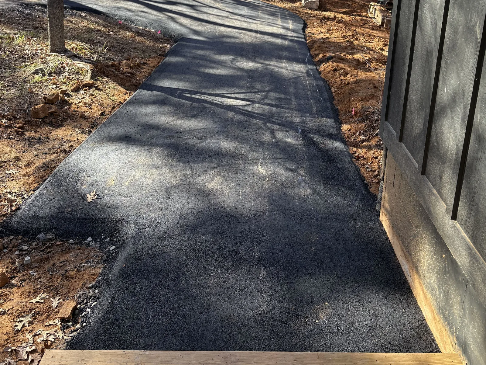 New asphalt walk and pad running alongside a dark cabin to a wooden deck