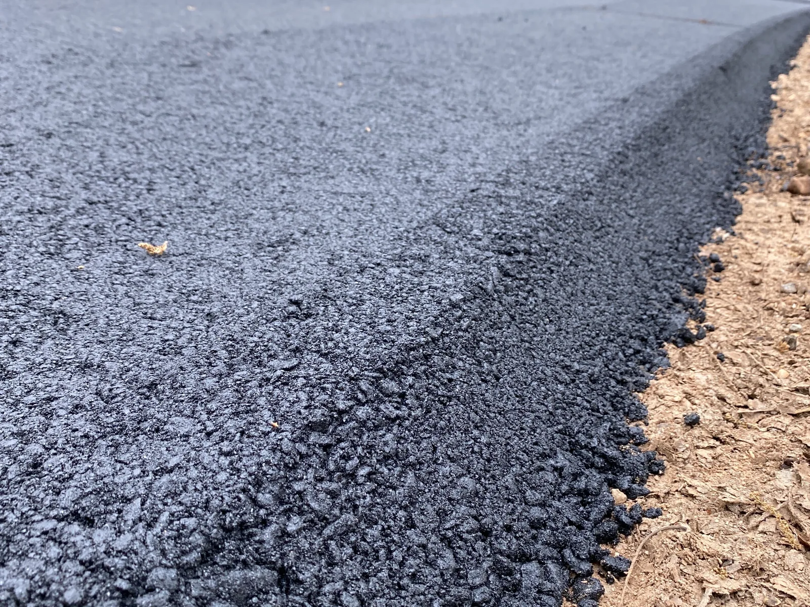 Close view of a fresh asphalt edge sitting on a crushed stone shoulder