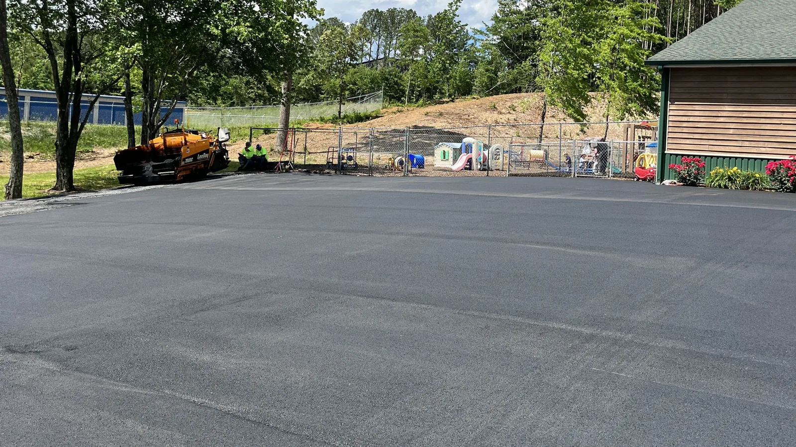 Wide sheet of new asphalt at a commercial property with the paver parked at the edge