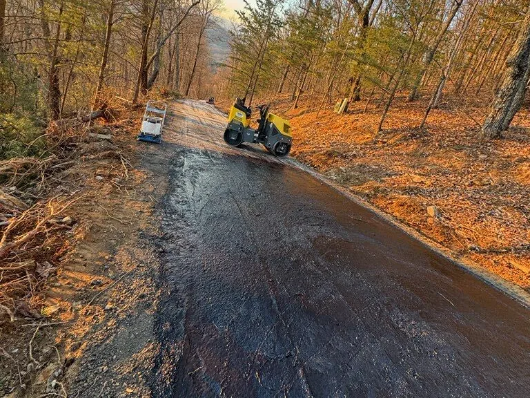 Roller working a fresh asphalt lane through the woods in evening light