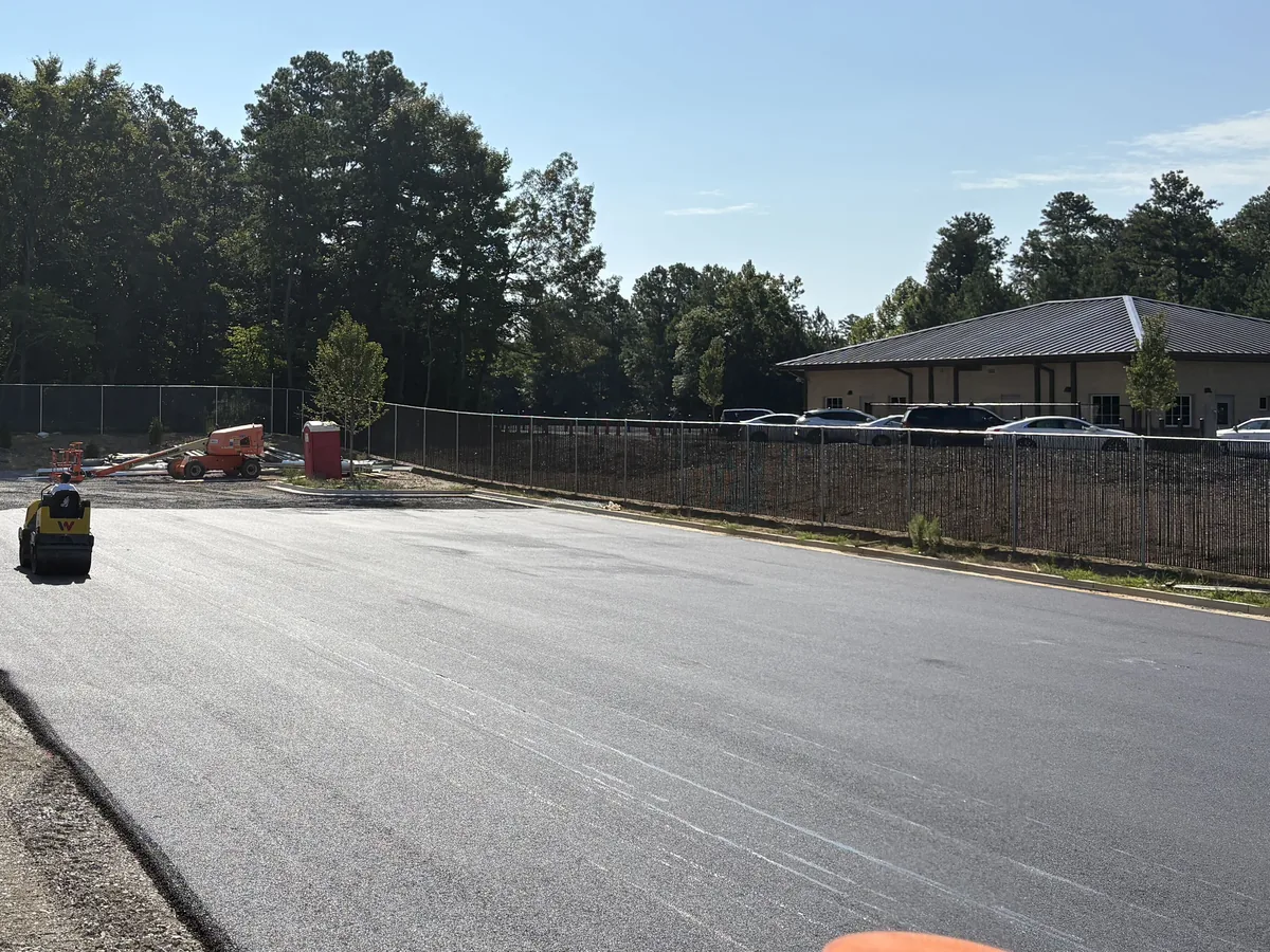Freshly laid asphalt parking lot at a metal building with a roller finishing the surface
