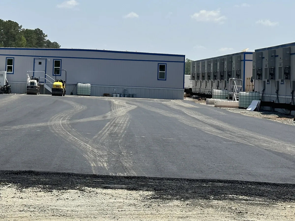 New asphalt parking lot beside modular buildings with a roller and paver on the fresh mat