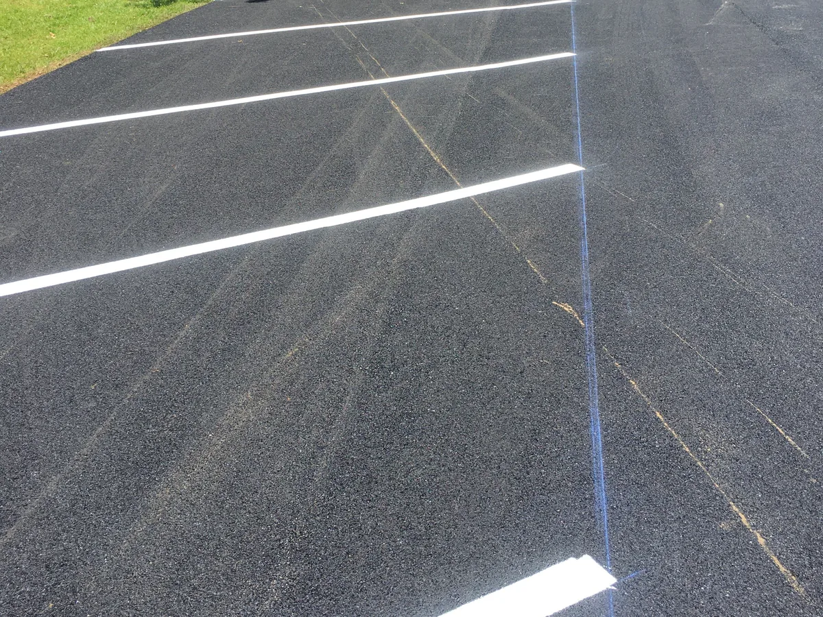 Chalk line snapped across new asphalt beside a freshly painted parking stripe