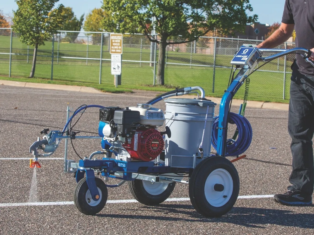 Walk-behind striping machine laying a fresh white line across an asphalt lot