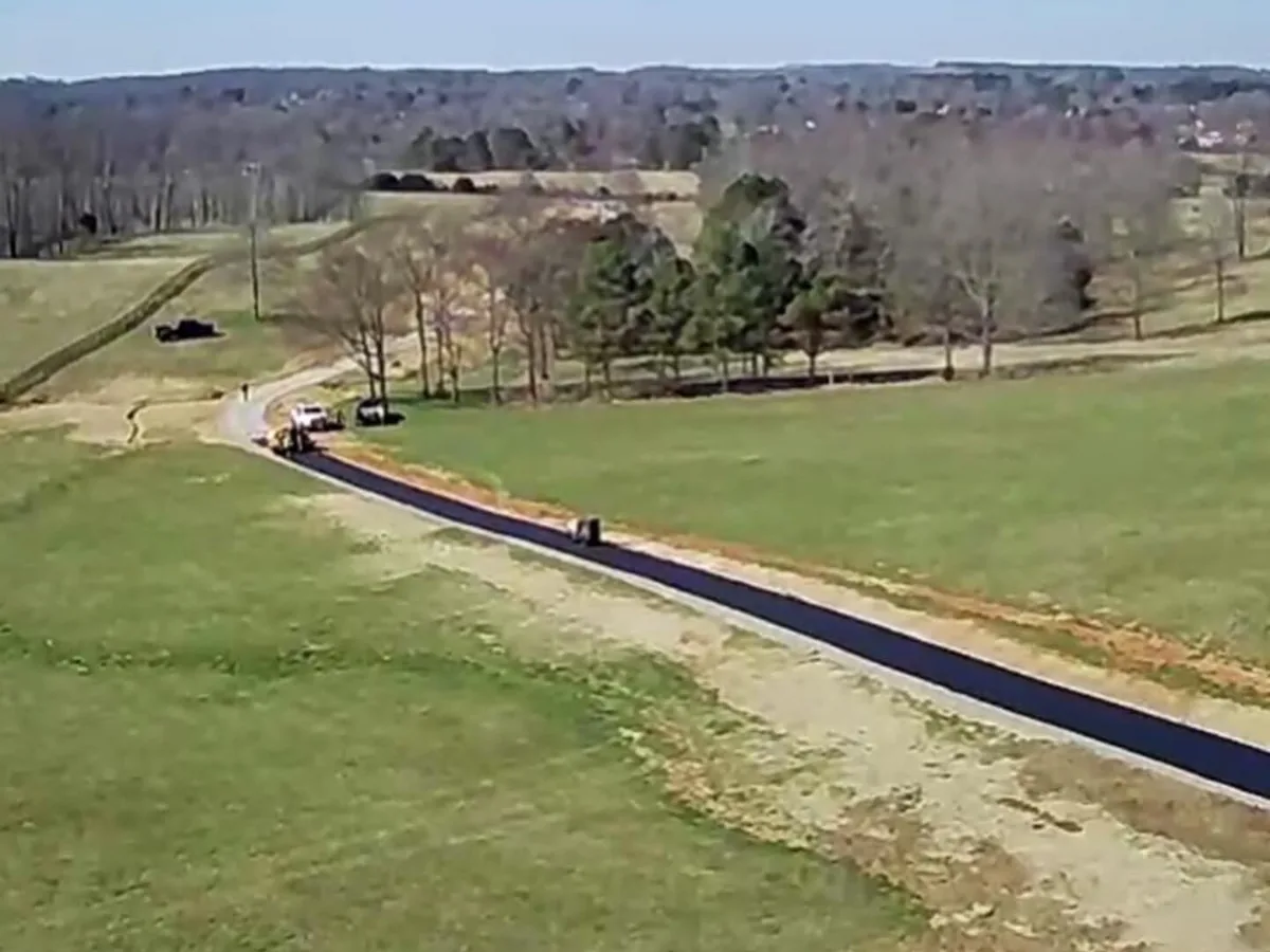 Aerial view of a long new asphalt lane being paved across rolling pasture