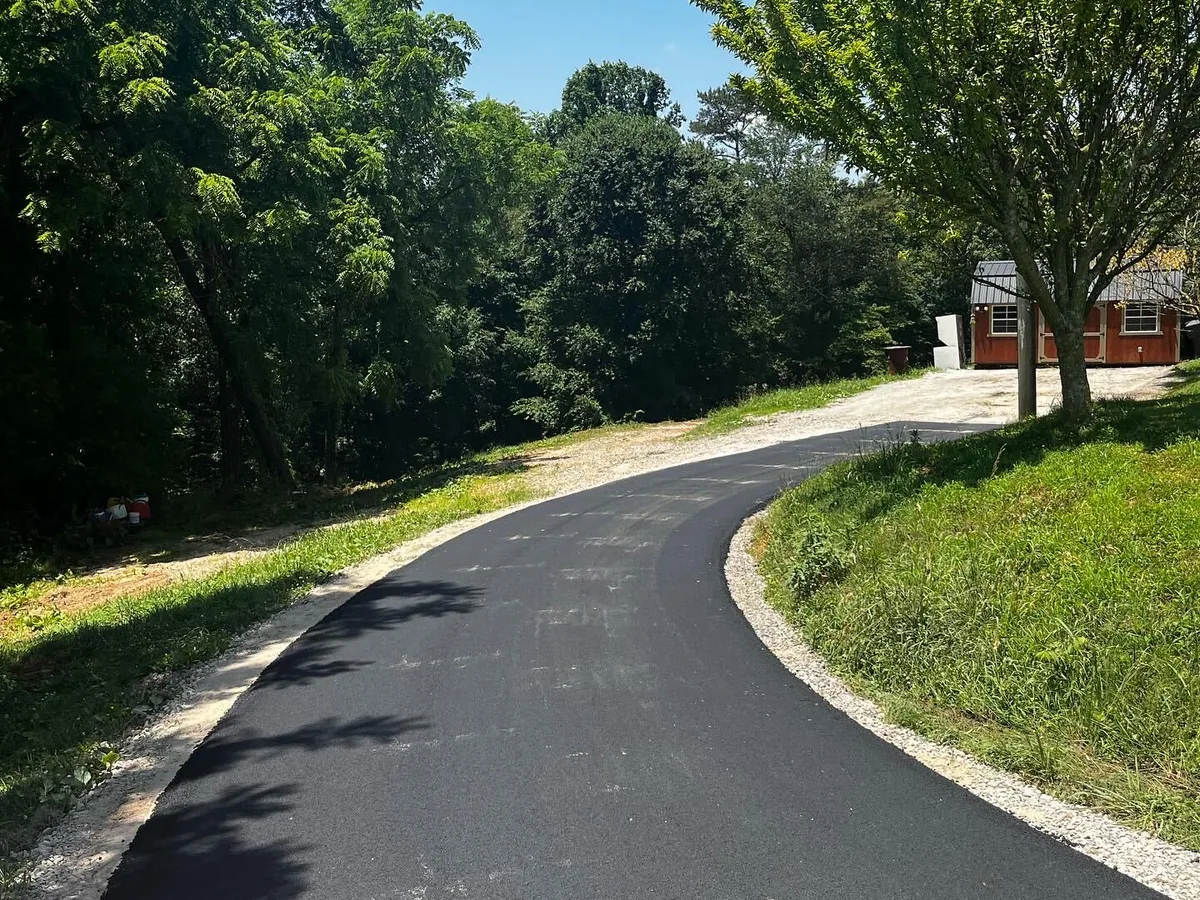 Curving asphalt lane with a crisp gravel shoulder climbing past a grassy bank
