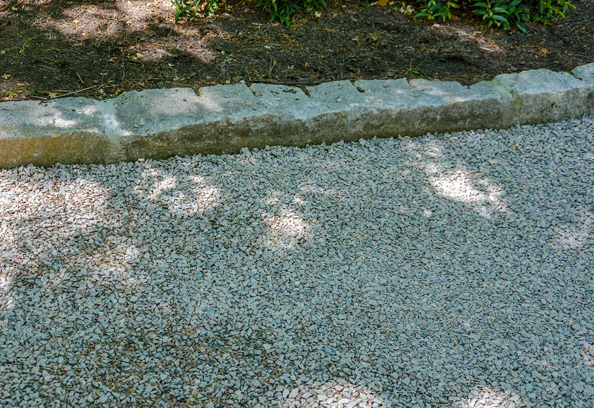 Close-up of a chip seal surface showing the stone chips locked into the asphalt binder at a stone edge